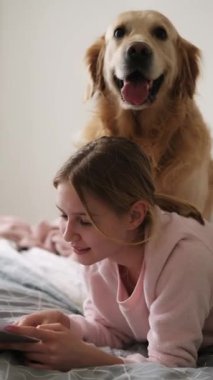 Yatak odasında köpekle Not Defteri okuyan sevimli küçük kız, dikey video.