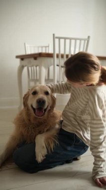 Mutlu genç kız, evde yerde sevimli bir köpeği kucaklıyor ve okşuyor. Dikey video.