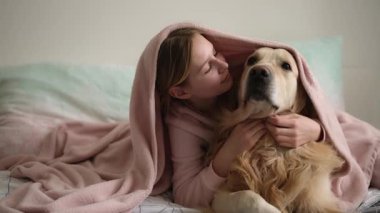 Tatlı küçük kız yatakta köpekle oynuyor ve battaniyenin altında sarılıyor.