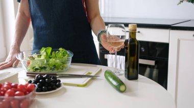 Genç kadın evde, mutfakta Yunan salatasını hazırlarken, ev yemeklerini kucaklarken beyaz şaraptan hoşlanıyor.