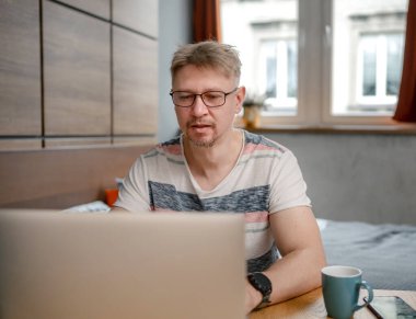 Adam evde, yatak odasında bilgisayarla uzaktan çalışıyor.