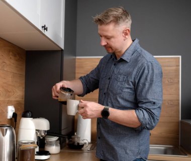 Yakışıklı adam mutfakta kendine kahve dolduruyor.