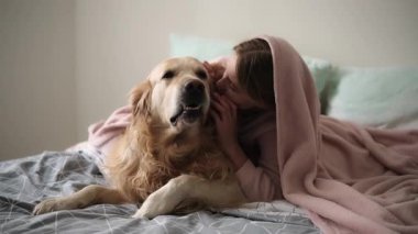 Tatlı küçük kız yatakta bir köpekle oynuyor, battaniyenin altında mutlu bir şekilde sarılıyor.
