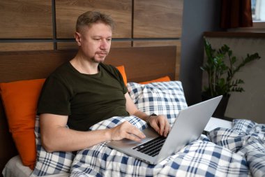 Adam sabahları evinde dizüstü bilgisayarla yatakta yatıyor.
