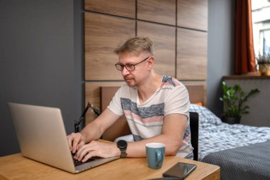 Adam evde, yatak odasında bilgisayarla uzaktan çalışıyor.