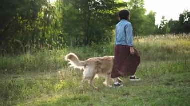 Güzel bir kadın arka plandan yavaş çekimde tasmalı bir köpeği gezdirir.