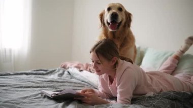 Yatak odasında köpekle Not Defteri okuyan tatlı küçük kız.