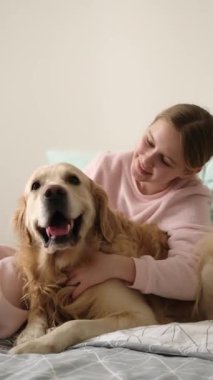 Sevimli küçük kız neşeyle yatakta güzel bir köpekle oyun oynuyor, dikey video.