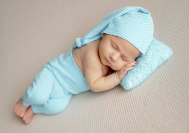 Yeni doğmuş bir bebeğin turkuaz şapkayla ve pantolonla uyumasının stüdyo fotoğrafı.