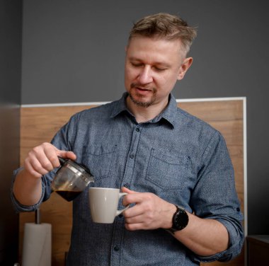 Yakışıklı adam mutfakta kendine kahve dolduruyor.