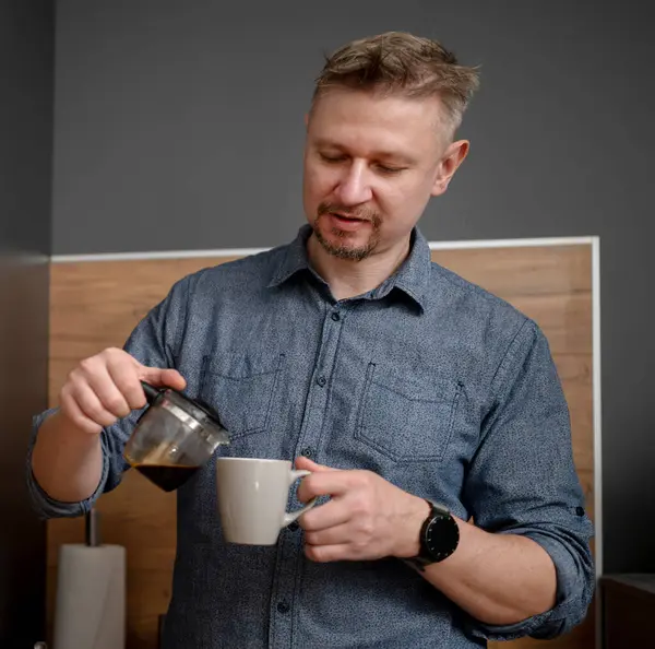 Yakışıklı adam mutfakta kendine kahve dolduruyor.