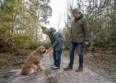 Baba ve kızı İlkbaharda altın bir av köpeğiyle ormanda yürüyorlar.