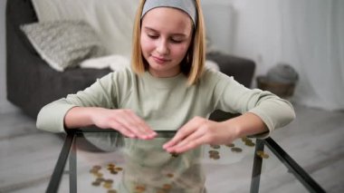 Sevimli küçük kız, çocukluktan kalma finansal edebiyat kavramını gösteren cam bir masaya para sayıyor.