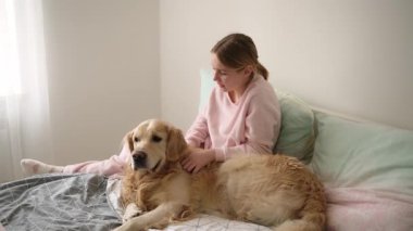 Sevimli küçük kız sevişiyor ve yatakta altın köpekle oynuyor.