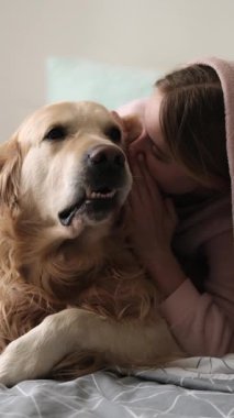 Küçük tatlı kız yatakta köpekle oynuyor ve battaniyenin altında sarılıyor.