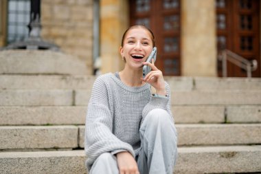 Merdivenlerde oturan, telefonda konuşan mutlu kız.