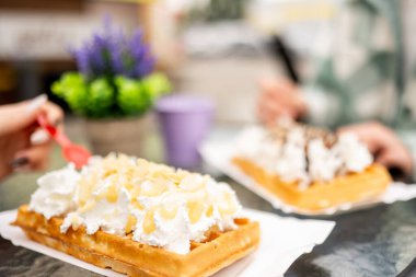 Belçika Waffle 'ının tadını çıkaran iki kız yakın plan, yumuşak odaklı bir kafede.