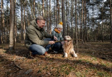 Baba ve kızı İlkbaharda altın bir av köpeğiyle ormanda yürüyorlar.
