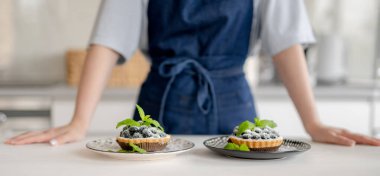 Mutfakta hazırlanmış yaban mersinli pastaların önünde duran kız.