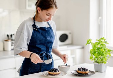 Ev Mutfağında Yaban mersinli böreğin üzerine pudra şekeri serpiştiren kız.