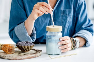 Mutfakta, hazırlanmak için aksesuarların yanında mavi buzlu kibrit Latte içen bir kadın.