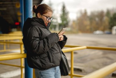 Otobüs durağında otobüs beklerken Smartphone 'a bakan kız