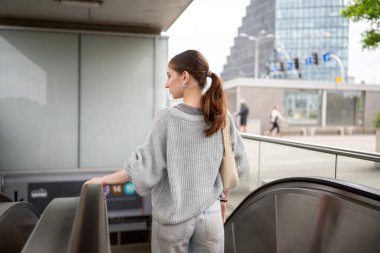 Metroyla yürüyen merdivenden inen genç bir kadın.