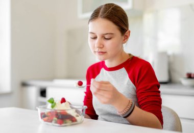 Gülümseyen kız mutfakta meyve salatası yiyor.