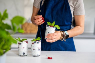 Mutfakta yoğurtlu Chia tohumu ve böğürtlenle tatlı yapan bir kadın.