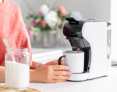 Evdeki kahve makinesinde kahve yapan bir kadının yakın çekimi.