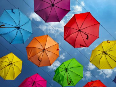 Parlak, çok renkli, açık şemsiyeler, güneş tarafından aydınlatılmış, mavi gökyüzüne karşı asılı.