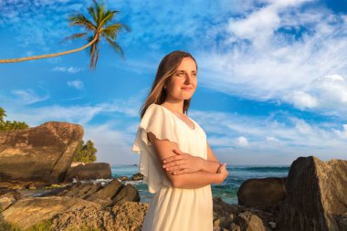 Portriat 'ta beyaz elbiseli güzel bir kadın denize yakın tropikal bir plajda kalıyor.