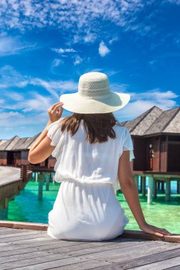 Maldivler adasındaki tropikal sahil iskelesinde (ahşap iskelede) su lüks villalarının önünde oturan güzel genç bir kadın.