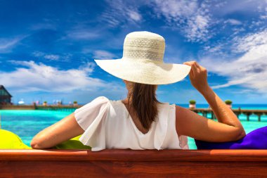 Güzel bir kadın güneşli bir yaz gününde lüks bir tropik plajda salıncakta oturuyor.