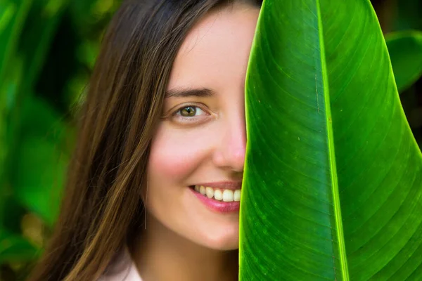 大きな熱帯の葉の後ろに隠れている美しい女性 — ストック写真