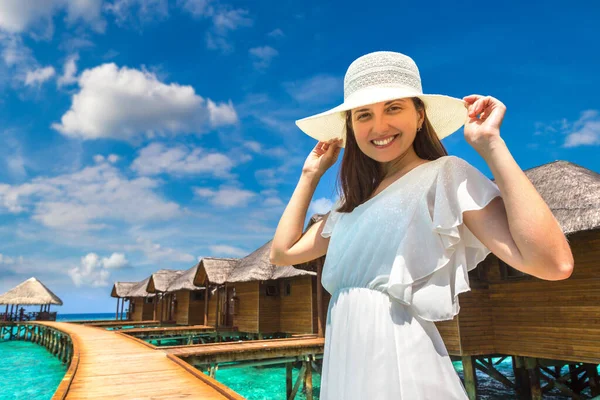 stock image Beautiful young woman in front of water luxury villas standing on the tropical beach jetty (wooden pier) in Maldives island