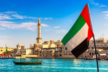 Abra 'ya karşı Birleşik Arap Emirlikleri bayrağına odaklan. Eski ahşap tekne ve Dubai Körfezi' ndeki Dubai Mescidi Camii.