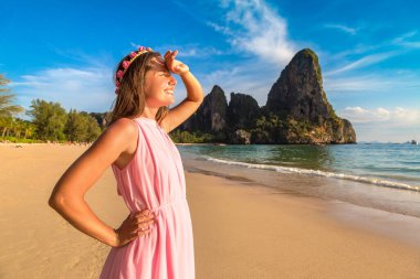 Pembe elbise giyen genç ve güzel bir kadın ve yüzü parlak güneş ışığıyla kaplı bir çiçek çelengi. Tropikal Railay Sahili, Krabi, Tayland