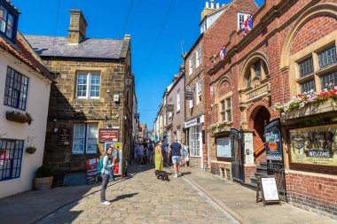 WHITBY, İngiltere - 13 Ağustos 2022: Whitby 'deki tipik turist caddesi - Güneşli bir yaz gününde popüler turizm beldesi, Kuzey Yorkshire, İngiltere