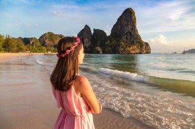 Genç ve güzel bir kadın pembe elbise giyiyor ve tropikal Railay Sahili 'nde çiçek çelengi, Krabi, Tayland