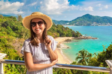 Güneşli bir günde Tayland 'ın Phuket Adası' ndaki Laem Sing plajının panoramik hava manzarasında mavi elbise ve hasır şapka giyen kadın gezgin.