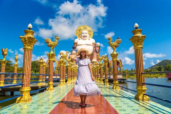 サムイ島のワット プライ ラーム寺院にある巨大な笑顔や幸せな仏像で青いドレスと藁帽子を身に着けている女性旅行者 — ストック写真