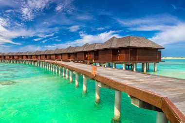 Su Villaları (Bungalovlar) ve yaz günü Maldivler 'deki tropik sahildeki ahşap köprü