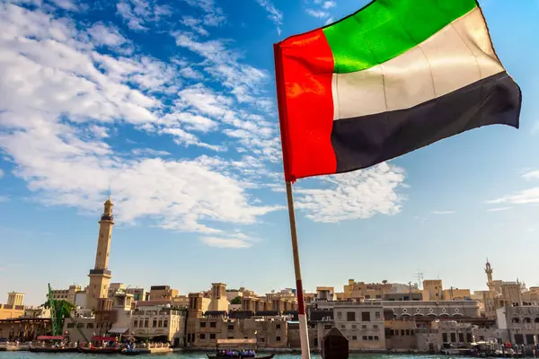 Focus on a flag of   United Arab Emirates flag against  bay Creek and Grand Bur Dubai Masjid Mosque in Dubai, United Arab Emirates