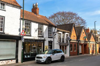 BEVERLEY, İngiltere - 11 Nisan 2025: White Mini Cooper İngiltere 'nin Yorkshire, İngiltere' nin Doğu Biniciliği 'ndeki Beverley' de yerel dükkanların bulunduğu eski tuğla ve kereste binalarının yakınına park etti