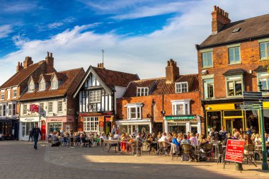 BEVERLEY, İngiltere - 11 Nisan 2025: Güneşli bir günde İngiltere 'nin Yorkshire, İngiltere' nin Doğu Biniciliği 'ndeki Beverley Tarihi Kent Merkezi' nde açık hava masalarında insanların yemek yediği sokak kafesi