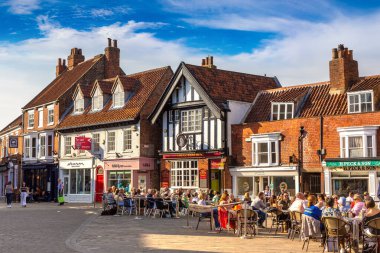 BEVERLEY, İngiltere - 11 Nisan 2025: Güneşli bir günde İngiltere 'nin Yorkshire, İngiltere' nin Doğu Biniciliği 'ndeki Beverley Tarihi Kent Merkezi' nde açık hava masalarında insanların yemek yediği sokak kafesi