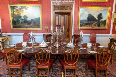 YORKSHIRE, İngiltere - 30 Haziran 2025: Kırmızı duvarlı, avizeli ve İngiltere, Kuzey Yorkshire 'daki Howard Kalesi' ndeki sofra takımlı Opulent Crimson Yemek Odası