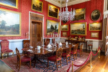 YORKSHIRE, İngiltere - 30 Haziran 2025: Kırmızı duvarlı, avizeli ve İngiltere, Kuzey Yorkshire 'daki Howard Kalesi' ndeki sofra takımlı Opulent Crimson Yemek Odası