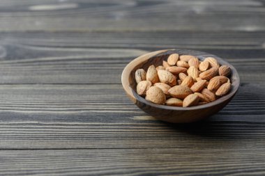 Kabuktaki çiğ badem ve badem kabukları koyu ahşap bir arka planda ahşap bir kasede. Fındık, beslenme ve çiğ gıda konsepti